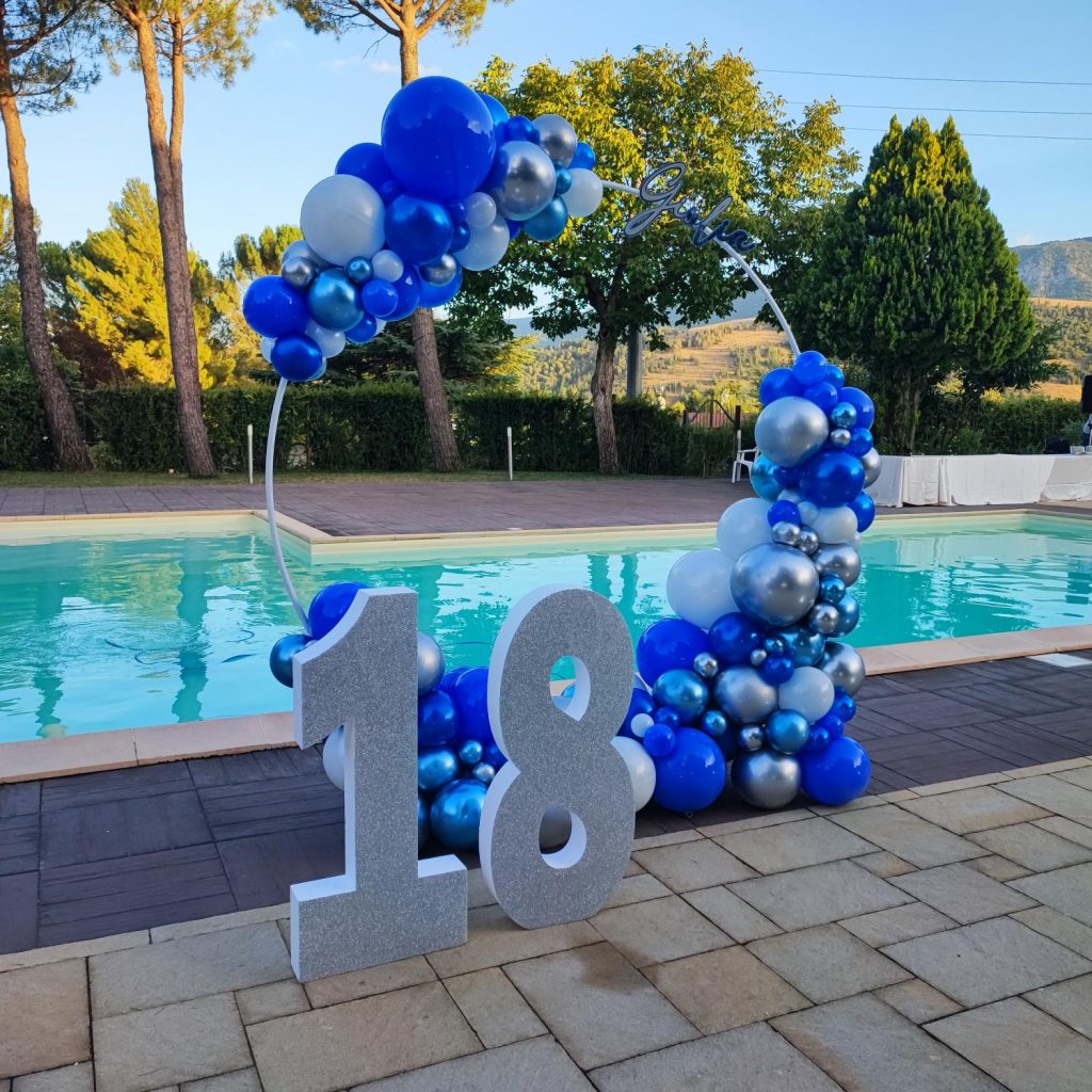 Composizione di palloncini blu e argento con numeri 18 glitterati a bordo piscina per un diciottesimo