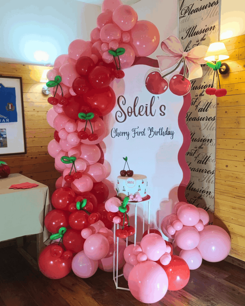 Allestimento con palloncini rossi e rosa a forma di ciliegie per un primo compleanno